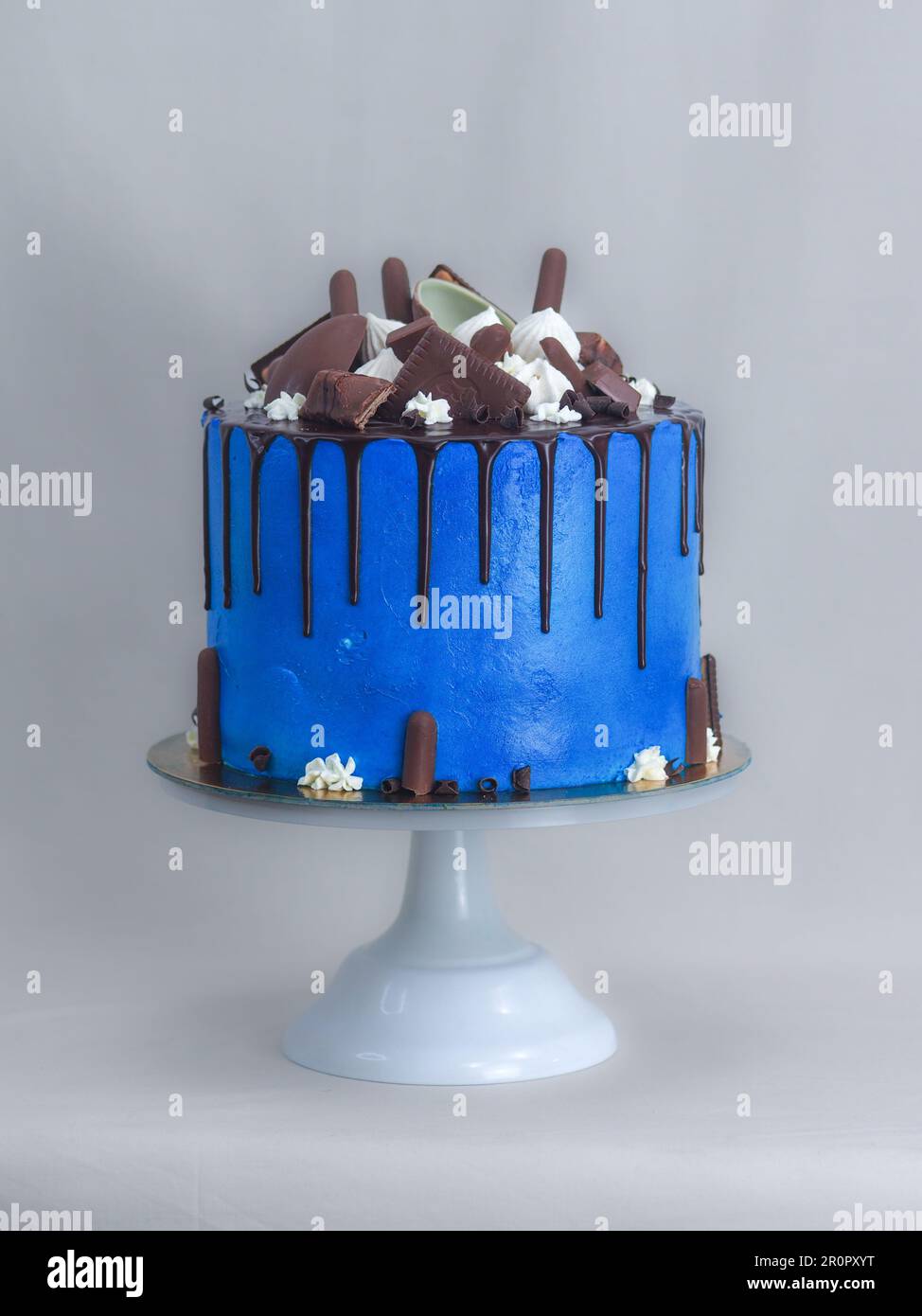 macro torta glassata blu primo piano con glassa al cioccolato fondente e dolci misti come guarnizione isolata su sfondo bianco per festeggiare Foto Stock