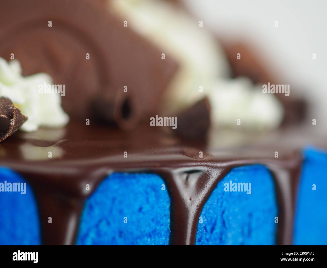 macro torta glassata blu primo piano con glassa al cioccolato fondente e dolci misti come guarnizione isolata su sfondo bianco per festeggiare Foto Stock