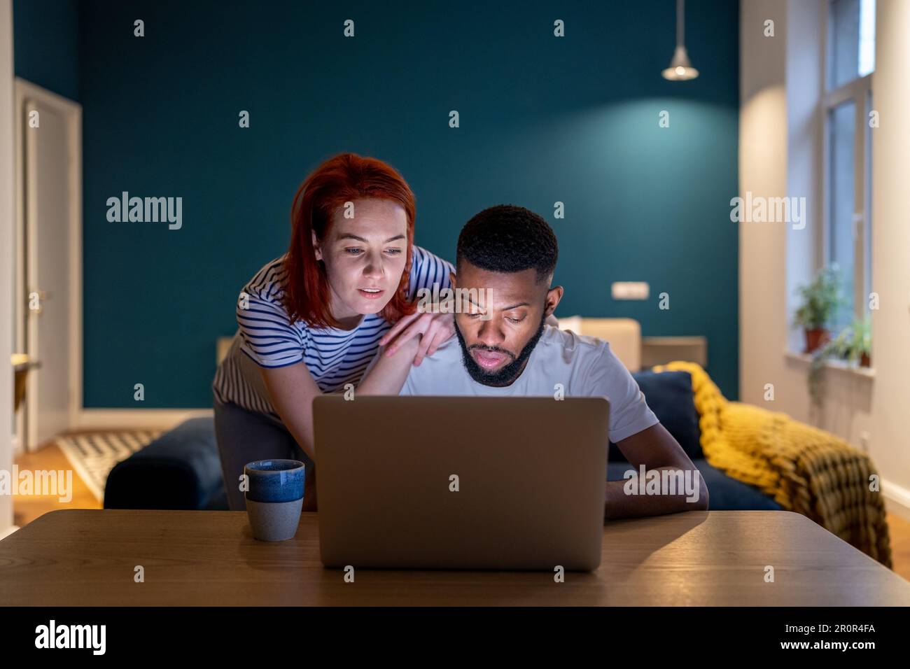 La moglie caucasica premurosa che sostiene il lavoro di abbraccio sul marito afro-americano del laptop. Foto Stock