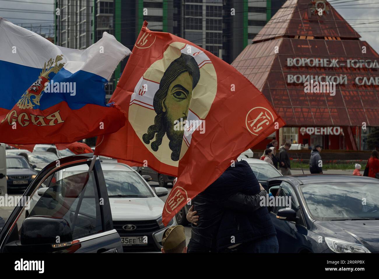 Gli uomini vedettero abbracciarsi sotto una bandiera rossa con Gesù Cristo il giorno della vittoria dell'Unione Sovietica sulla Germania nazista a Voronezh. L'evento è stato a lungo privatizzato dalle autorità ufficiali russe. Nel secondo anno della guerra con l'Ucraina, per le strade di Voronezh in questo giorno, sempre più simboli nazionalisti si mescolano a quelli sovietici. Le persone camminano per la città, divertirsi, cantare canzoni patriottiche e non ricordare l'essenza di quei terribili eventi a cui il 9 maggio è dedicato. (Foto di Mihail Siergiejevicz/SOPA Images/Sipa USA) Foto Stock