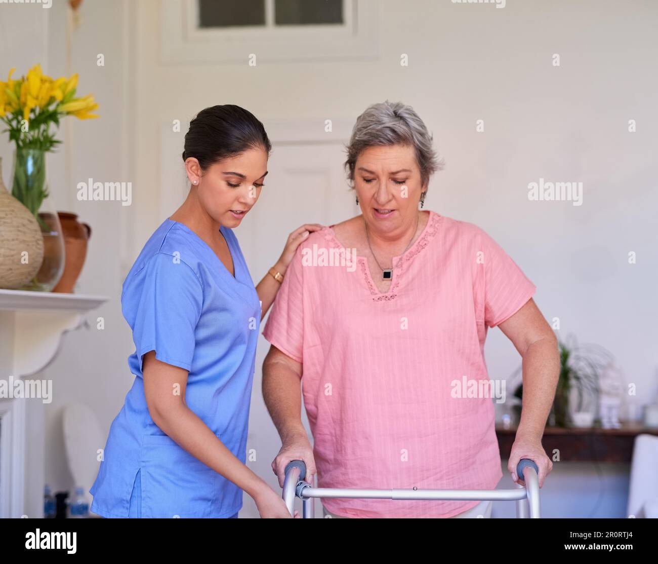 Passi lenti e costanti ora... un caregiver che assiste un paziente anziano con un camminatore in una casa di cura. Foto Stock