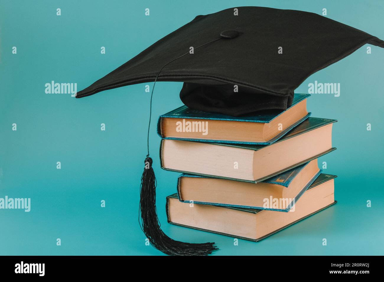 Cappellino di laurea con una pila di libri.Libri con cover stack e cappello da studente su sfondo blu. Conoscenza e Education. Libri insieme e letteratura e. Foto Stock