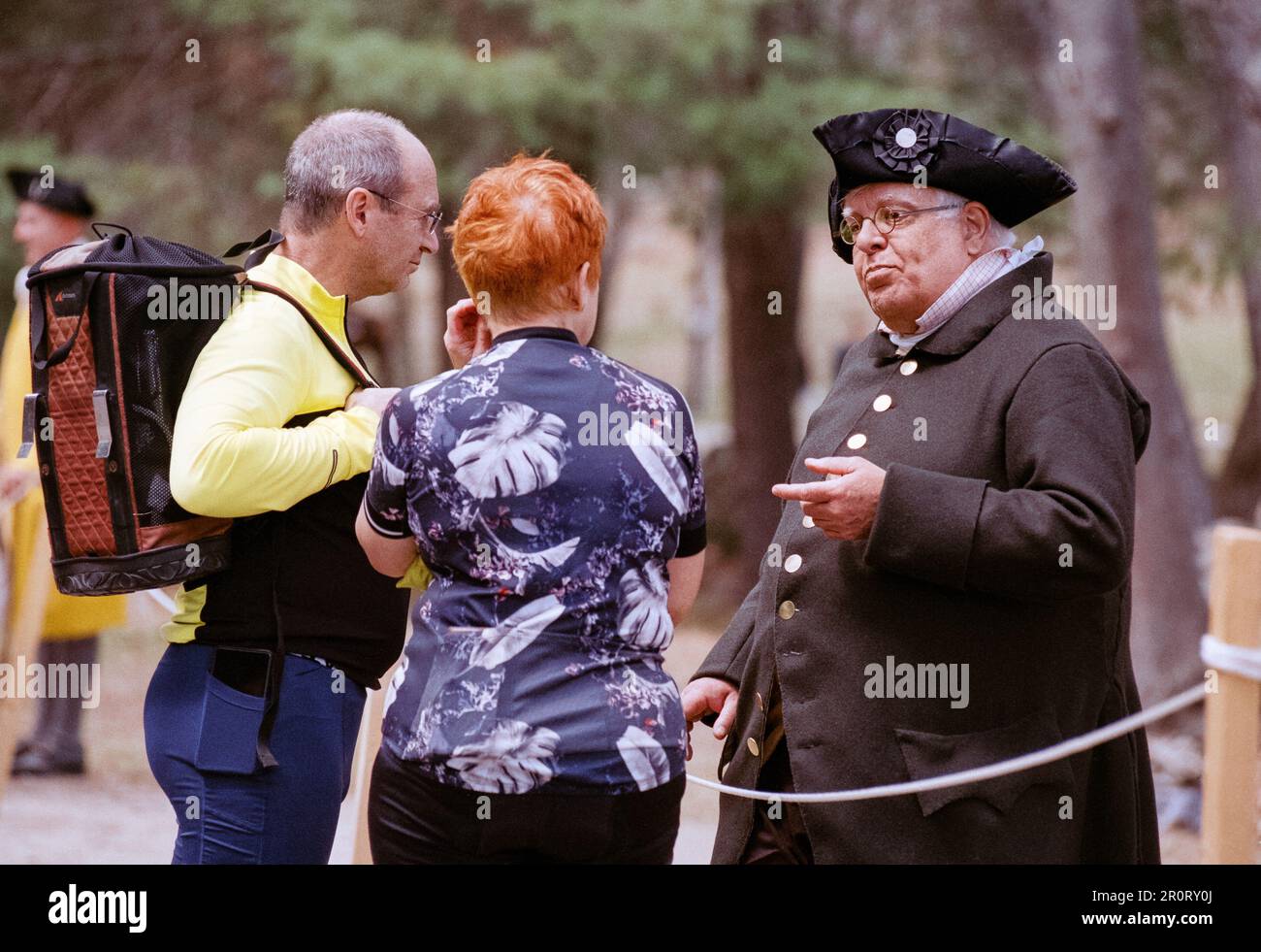 Lexington, Massachusetts USA - Aprile 2023 - due visitatori si fermano per parlare con un attore in abiti del periodo coloniale lungo Battle Road nel Minuteman Natio Foto Stock