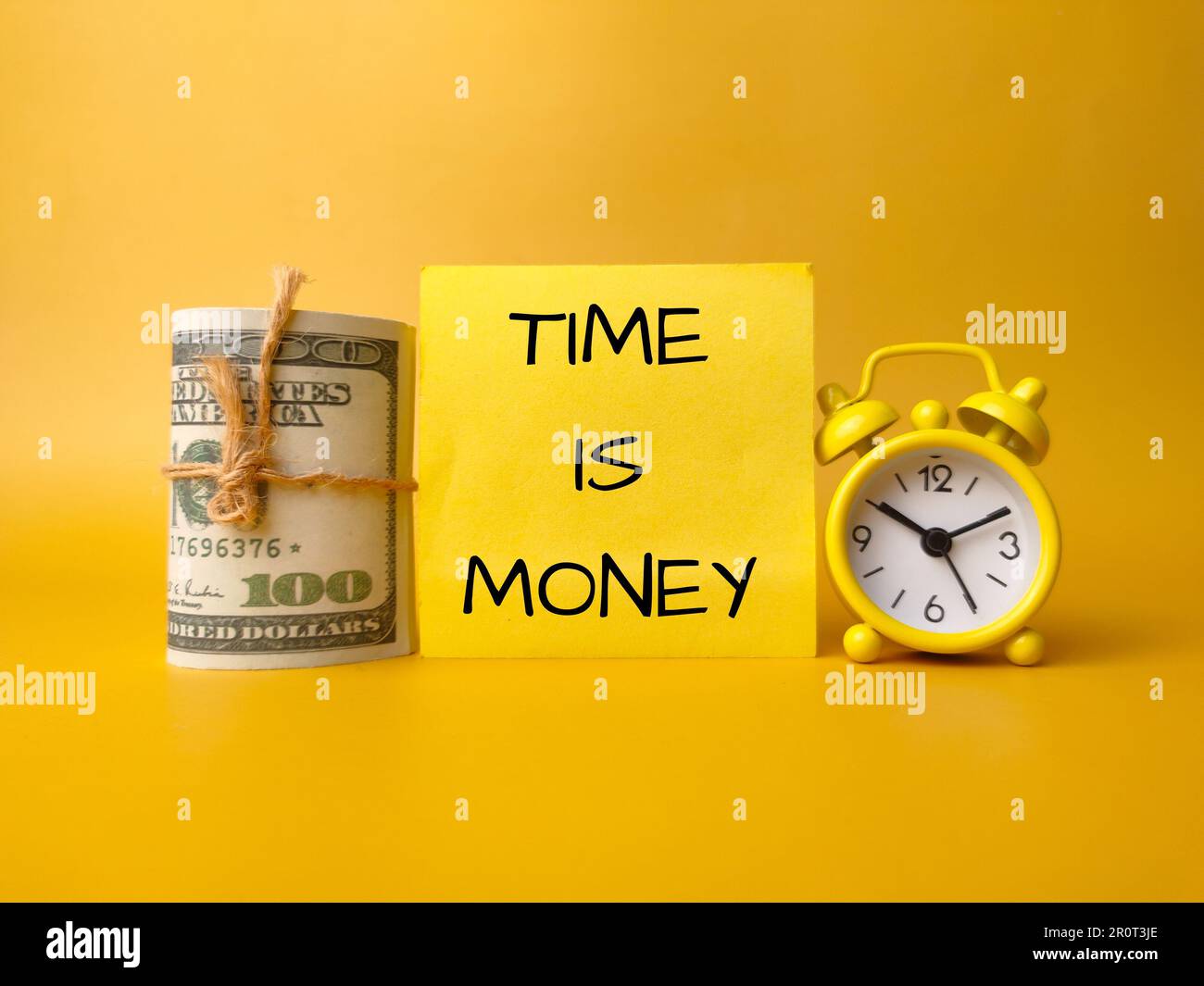Banconote e orologio con la parola TEMPO È DENARO su uno sfondo giallo Foto Stock