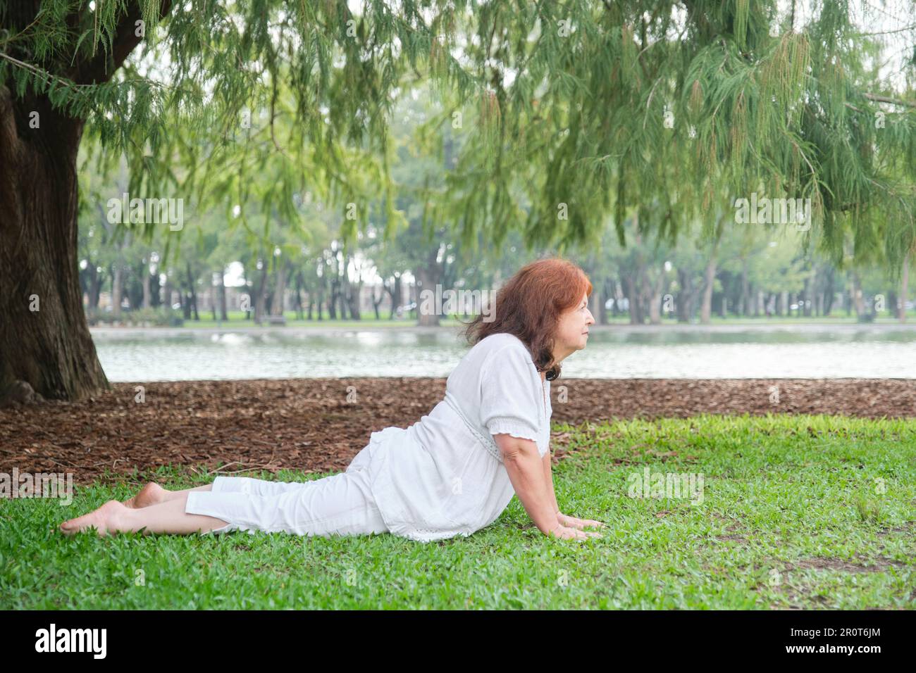 Donna latina matura in abiti bianchi praticando yoga in natura. Concetti: Benessere, vitalità, stile di vita attivo e sano. Foto Stock