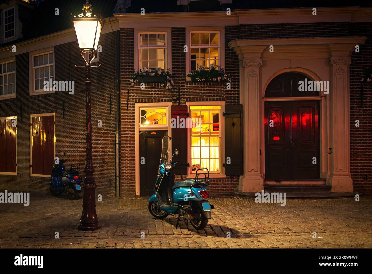 Vista del ciclomotore sotto il lampione illuminato sulla strada acciottolata di fronte alla casa residenziale di Amsterdam, Paesi Bassi. Foto Stock