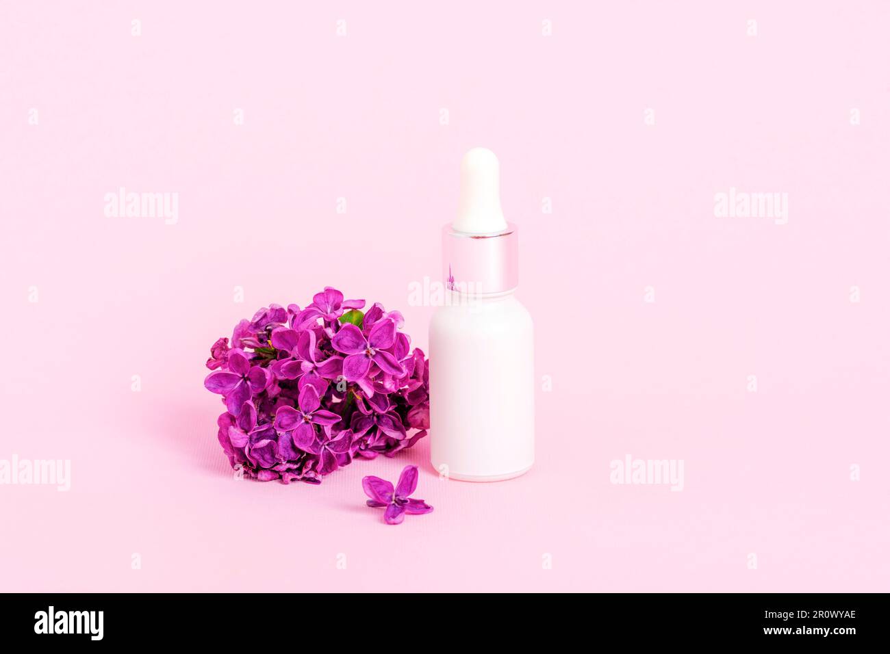 Bottiglia di siero bianco e fiori di lilla su sfondo rosa. Cura della pelle, cosmetica naturale concetto. Primo piano. Foto Stock