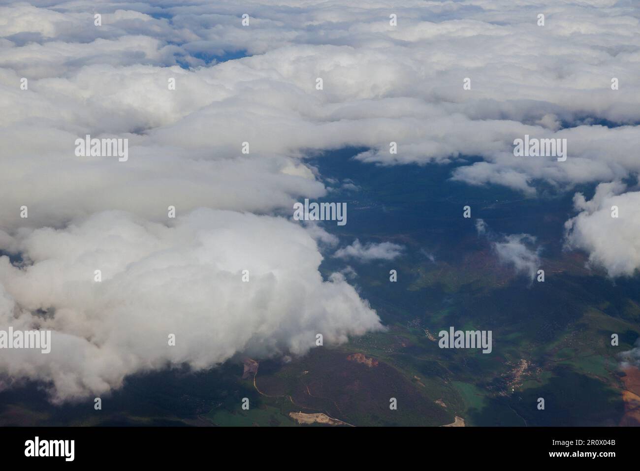 Una finestra dell'aeroplano offre la vista meravigliosa del paesaggio bello delle montagne verdi con le nuvole blu fluffy sullo sfondo Foto Stock