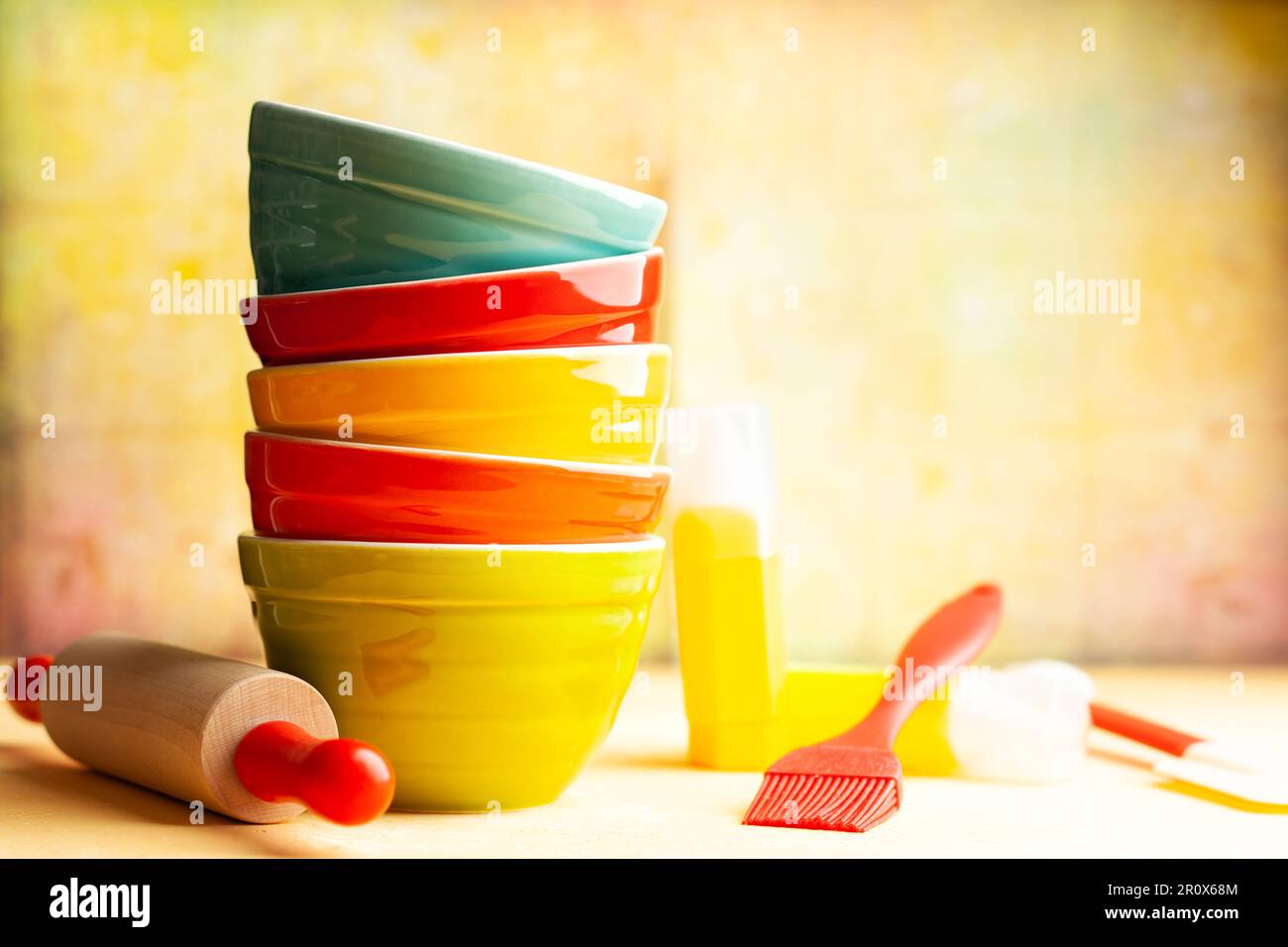 Utensili da cucina fondo con ciotole in ceramica multicolore, spilla, spatola su sfondo giallo. Concetto di arredamento cucina casa. Anteriore Foto Stock