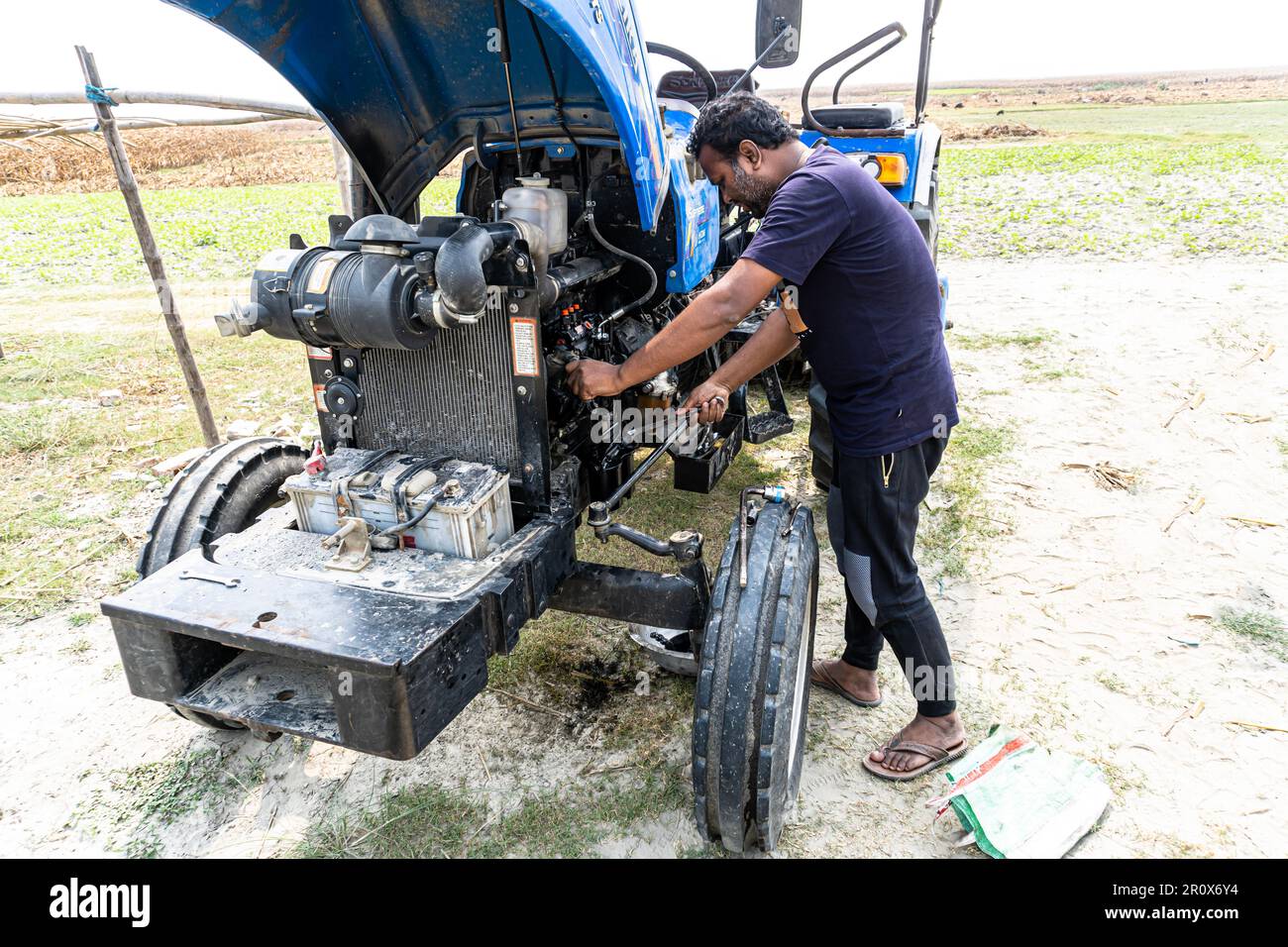 Vista ravvicinata dei tubi idraulici delle macchine per l'industria pesante. Aprire il cofano del trattore. Meccanico delle attrezzature agricole che lavora su un trattore blu Foto Stock