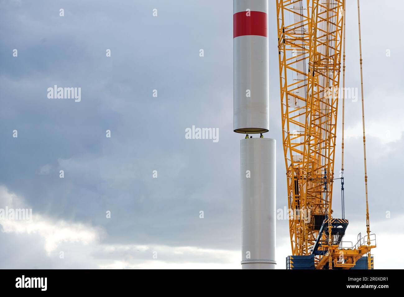 Crane sta spostando una parte di torre di una turbina eolica sul primo tubo guidato da persone all'interno, lavori di precisione nell'industria pesante, centrale elettrica per il rinnovo Foto Stock