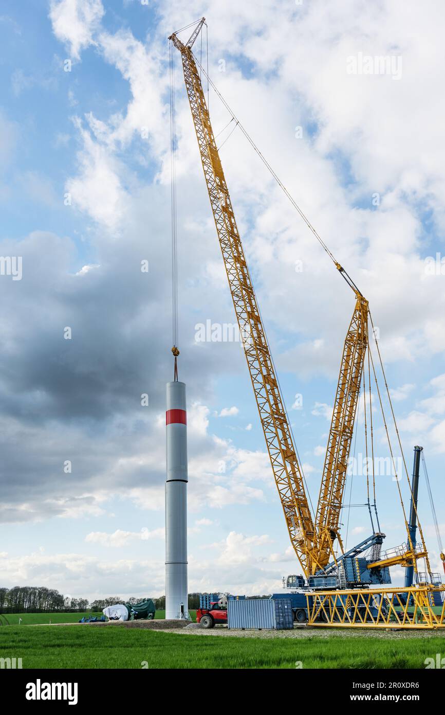 La gru gigante sta spostando una parte della torre dall'acciaio di una turbina eolica al primo tubo, sito di costruzione industriale pesante per una centrale elettrica rinnovabile Foto Stock