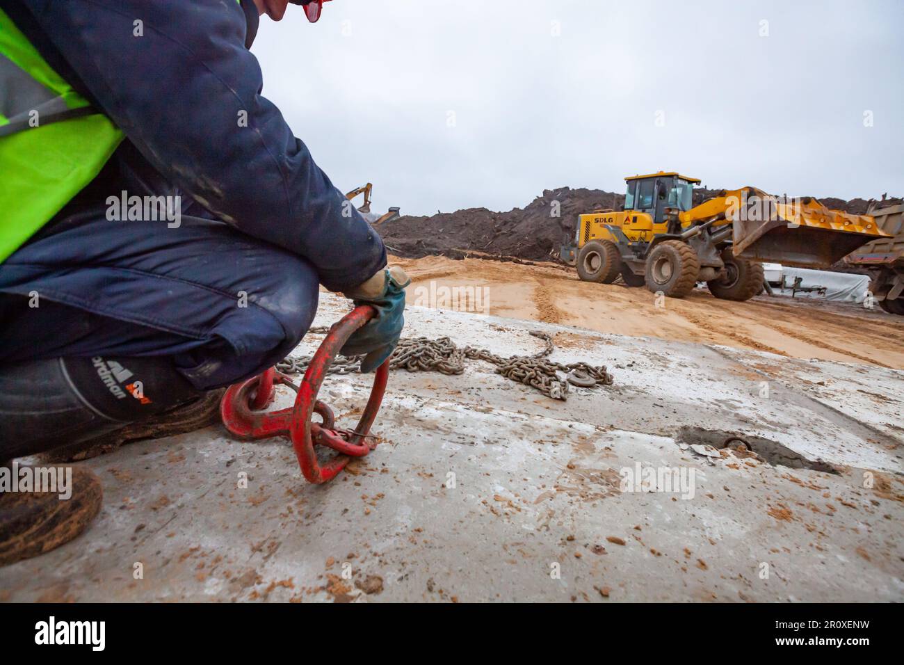 Ust-Luga, Leningrado oblast, Russia - 16 novembre 2021: Costruzione di strade in cemento. L'operatore installa le piastre in calcestruzzo utilizzando un gancio metallico con una catena. Nessun fac Foto Stock