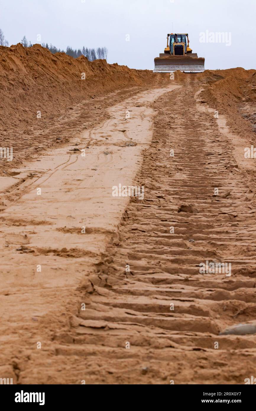 Stampe su sottobase e cingoli bulldozer. Cantiere stradale. Macchina sfocata sullo sfondo, primo piano a fuoco Foto Stock