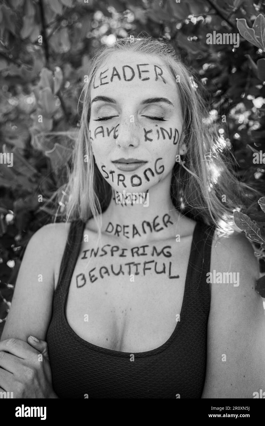 Una giovane donna con gli occhi chiusi e un'espressione premurosa con parole motivazionali scritte sulla pelle, foto in bianco e nero Foto Stock