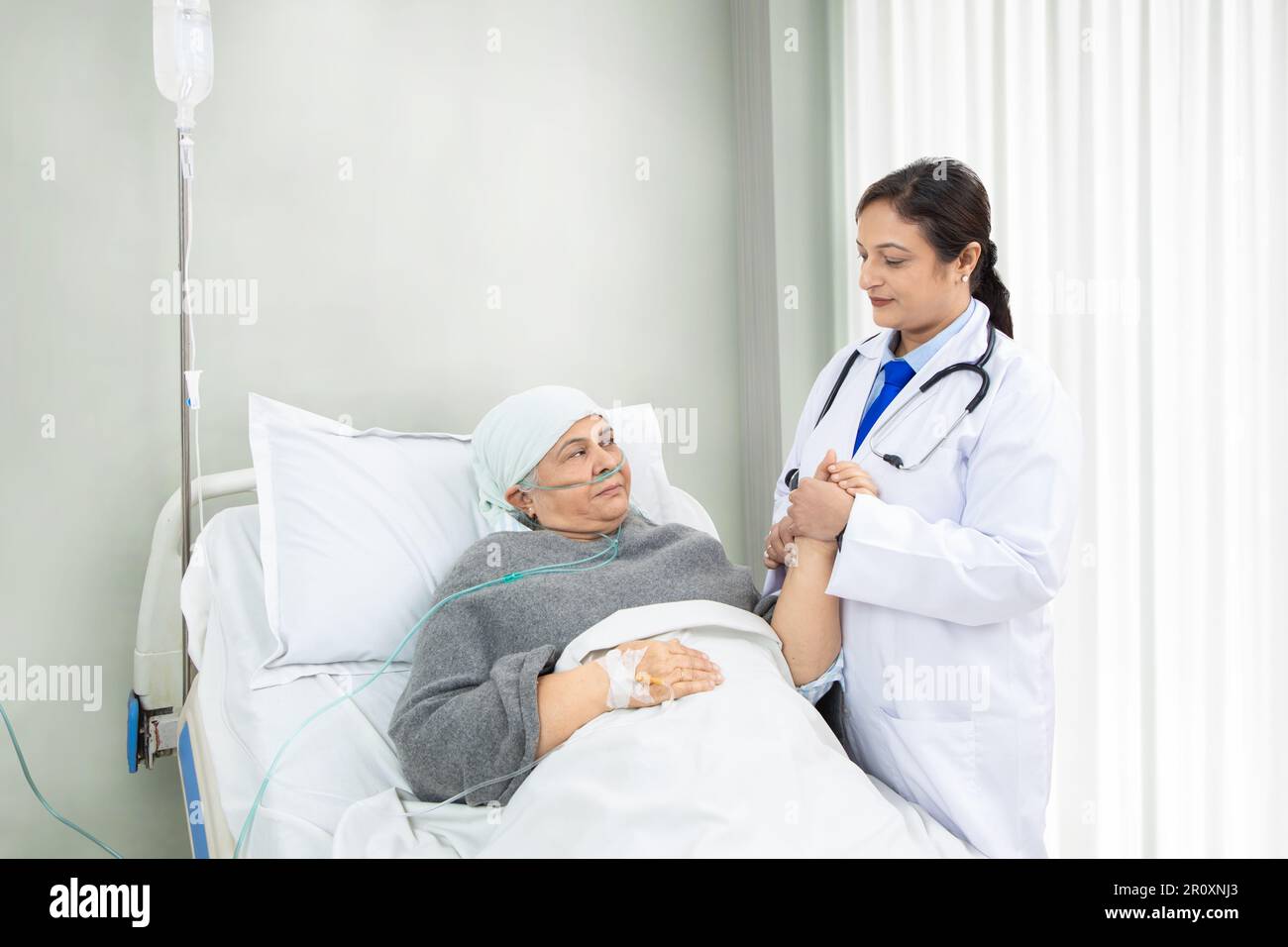 Medico indiano che tiene la mano del paziente anziano con la cannula nasale sdraiata nel letto dell'ospedale, la persona medica dà il supporto e la cura alla clinica, l'assistenza sanitaria con Foto Stock