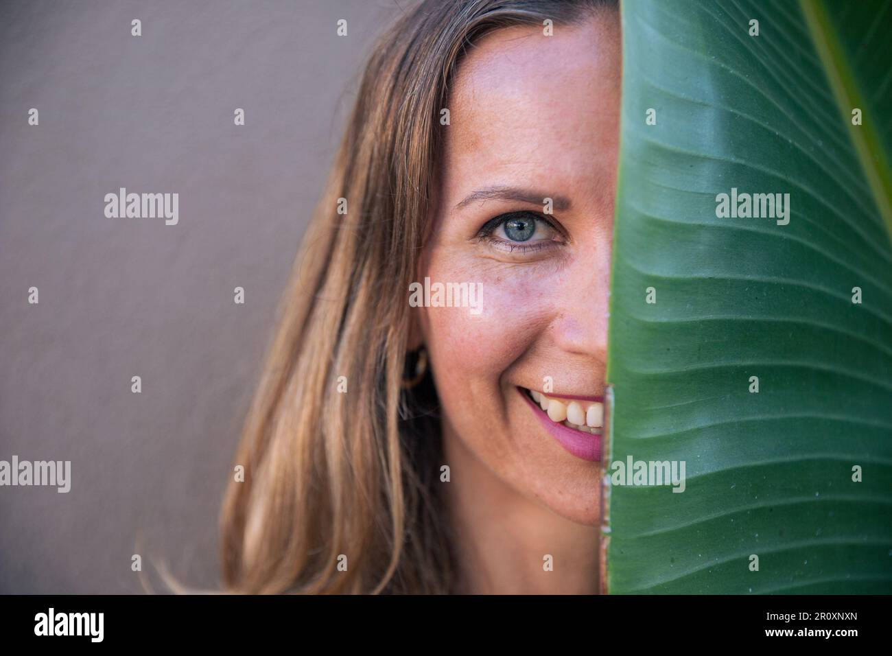 Ritratto di una donna sorridente con metà del suo volto nascosto dietro una foglia di banana. Foto Stock