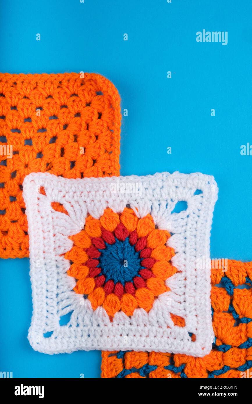 White Granny Square con motivo arancione centrale, rosso e blu. Due piazze Orange Granny dietro tutte su un Kingfisher Blue Backgraound. Foto Stock