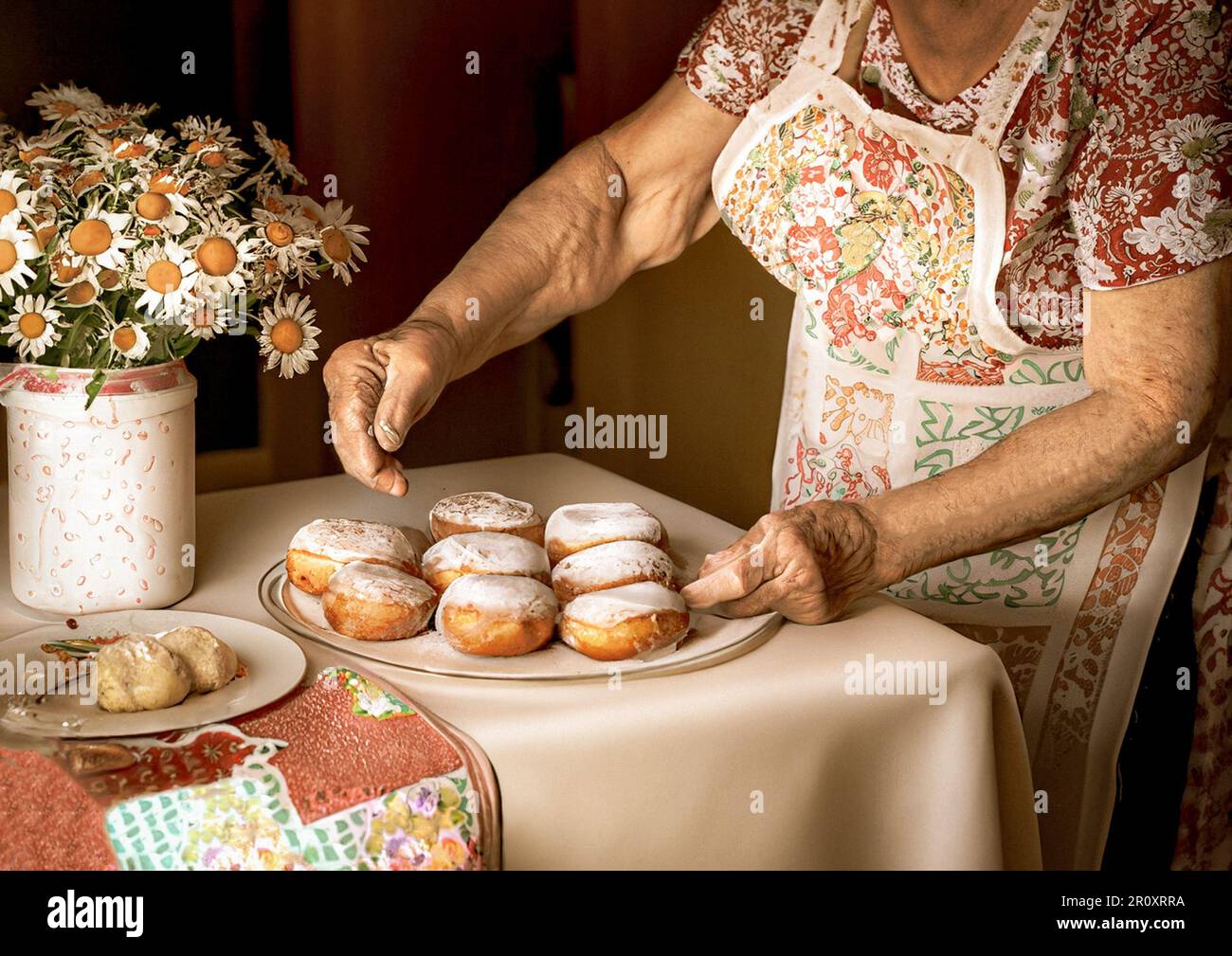 una vecchia signora che prepara ciambelle al tavolo della fattoria di legno Foto Stock