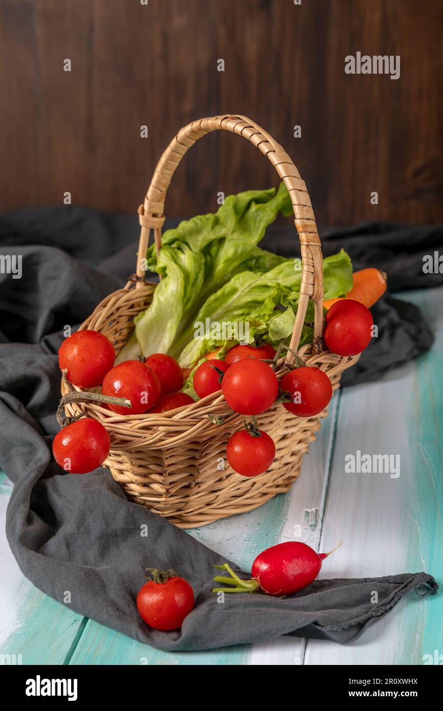 Un cestino di vimini contiene pomodori ciliegini rossi, lattuga e carote Foto Stock