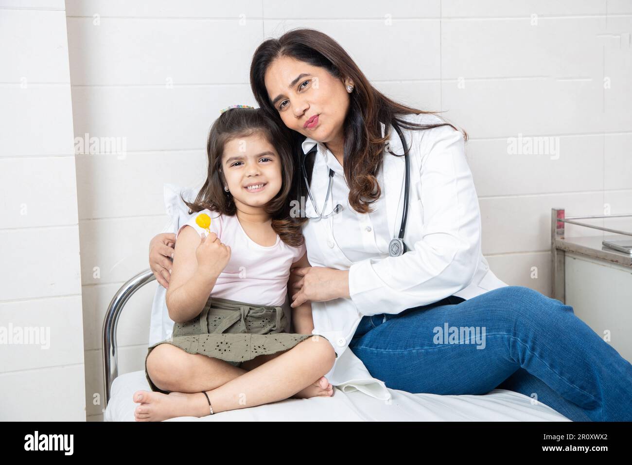 Felice bambina indiana ottenere lollipop da medico femminile a riunione in ospedale. Paziente bambino sorridente che festeggia il successo del trattamento con ge Foto Stock