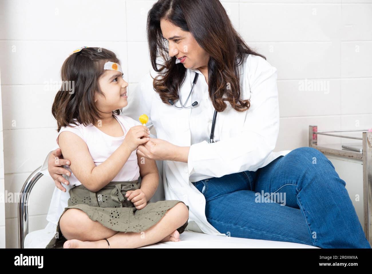 Medico generico indiano femmina dare lollipop a bambina paziente dopo il trattamento o il controllo in ospedale. Foto Stock