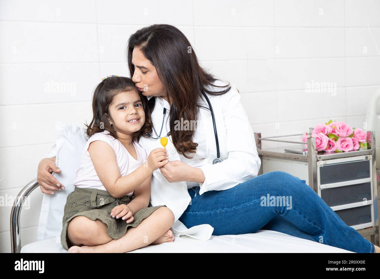 Felice bambina indiana ottenere lollipop da medico femminile a riunione in ospedale. Paziente bambino sorridente che festeggia il successo del trattamento con ge Foto Stock