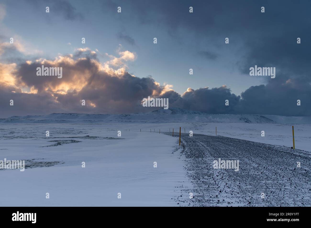 Vista panoramica su un paesaggio innevato di lava, rocce e montagne con stretta strada sterrata in Islanda durante l'inverno con sole luminoso Foto Stock