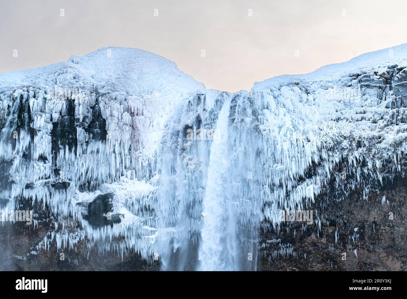 Vista ravvicinata della cima della cascata Seljandsfoss nel sud dell'Islanda durante l'inverno, coperta di neve e di spessi strati di ghiaccio dallo spruzzo Foto Stock