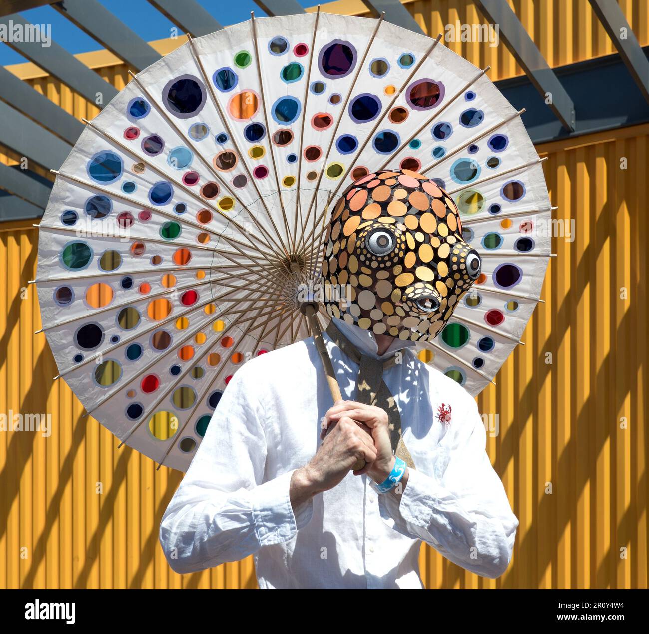 Uomo in una maschera di creatura marina, con un ombrello con cerchi tagliati colorati, sulla passeggiata Riegelmann Boardwalk durante la Coney Island Mermaid Parade. Foto Stock