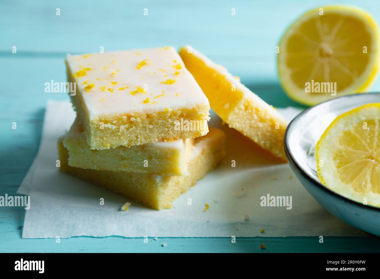 Brownie al limone con glassa al limone e scorza su carta da forno su fondo acquamarina Foto Stock