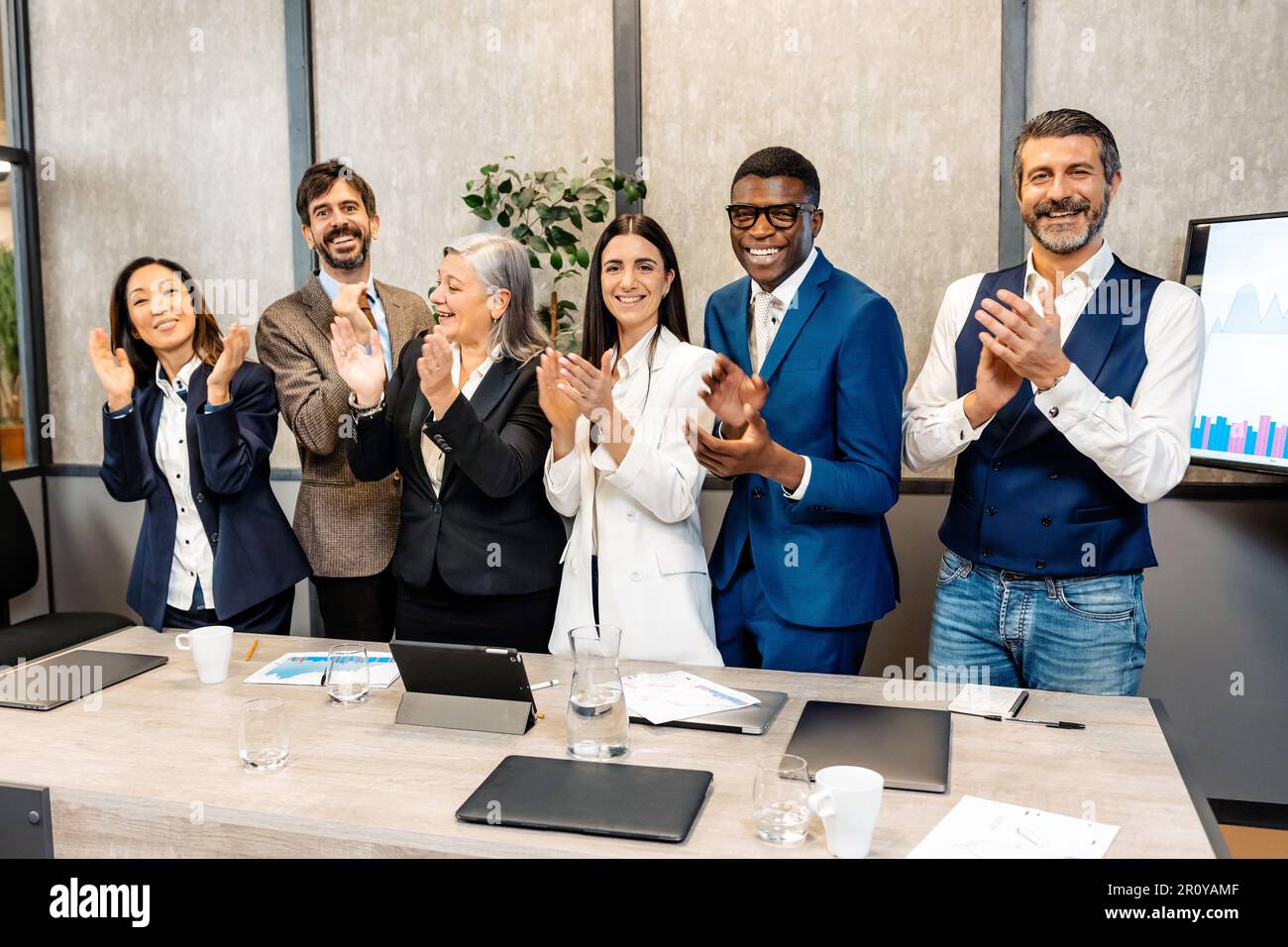 Gruppo di colleghi multietnici in formale indossare sorridente e lappare le mani durante la riunione in ufficio moderno Foto Stock