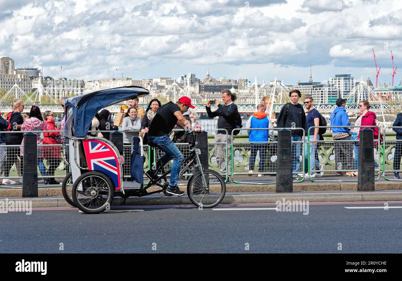 Un risciò di Londra o Pedicab che opera sul Ponte di Westminster affollato di turisti in un giorno di primavera soleggiato Londra centrale Inghilterra Gran Bretagna Regno Unito Foto Stock