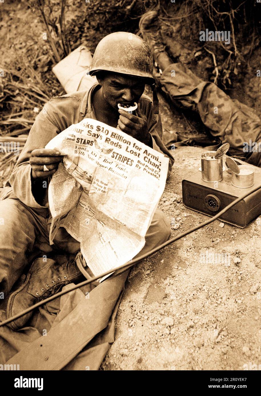 Pfc. Clarence Whitmore, voce operatore radio, xxiv Reggimento di Fanteria, legge le ultime notizie mentre godendo di chow durante il lull in battaglia, vicino Sangju, Corea. Il 9 agosto 1950. Foto di PFC. Charles Fabiszak, Esercito. (USIA) Foto Stock