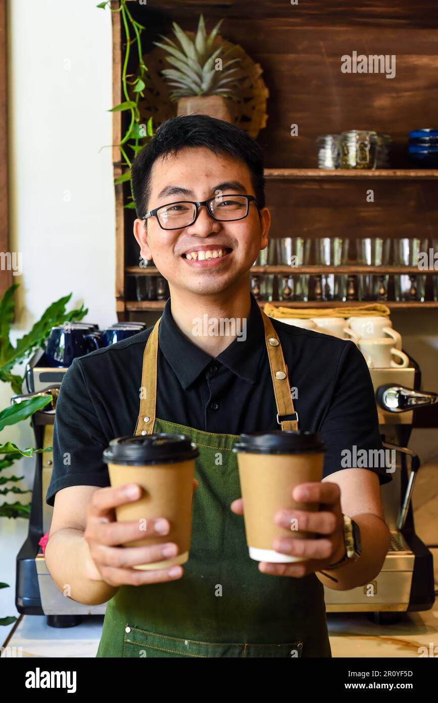 Cameriere vietnamita sorridente che tiene tazze di carta con caffè in un bar Foto Stock