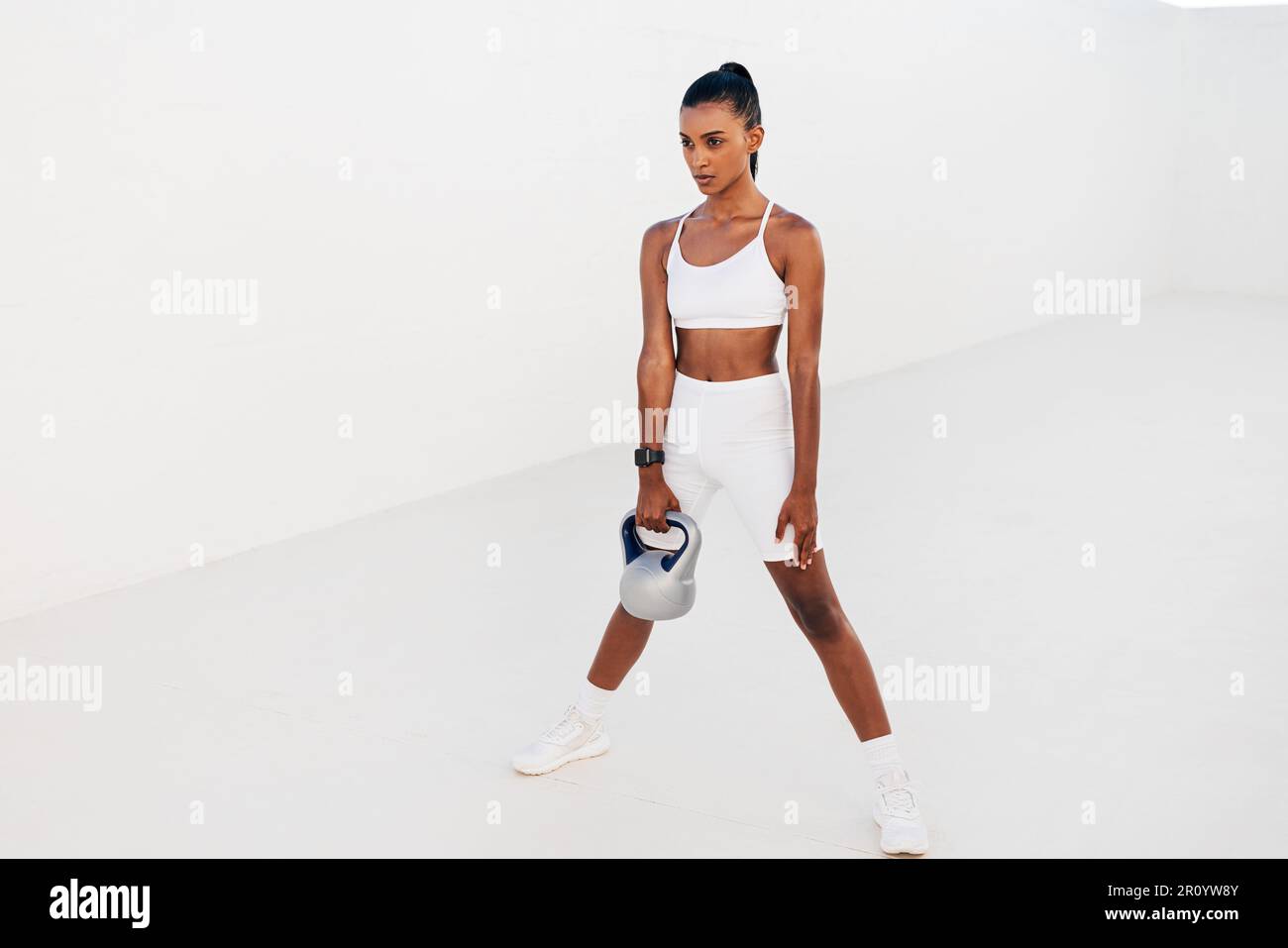 Donna in piedi con kettlebell all'aperto. Atleta femminile che si esercita con il peso in studio bianco all'aperto. Foto Stock