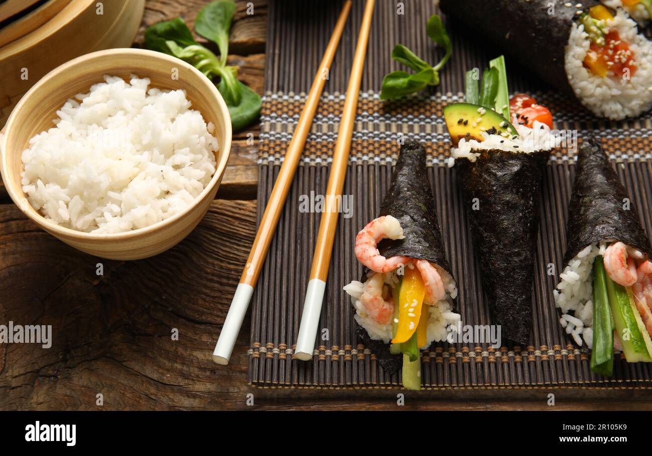Stuoia di bambù con gustosi coni di sushi, bacchette e riso bollito su  sfondo di legno, primo piano Foto stock - Alamy