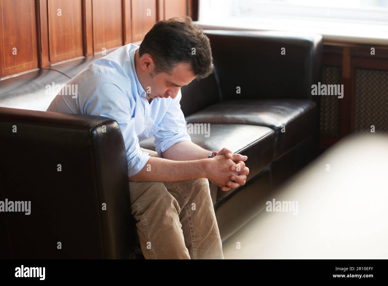 La testa è appesa bassa con tristezza... un uomo afflitto seduto su un divano con la testa appesa bassa. Foto Stock