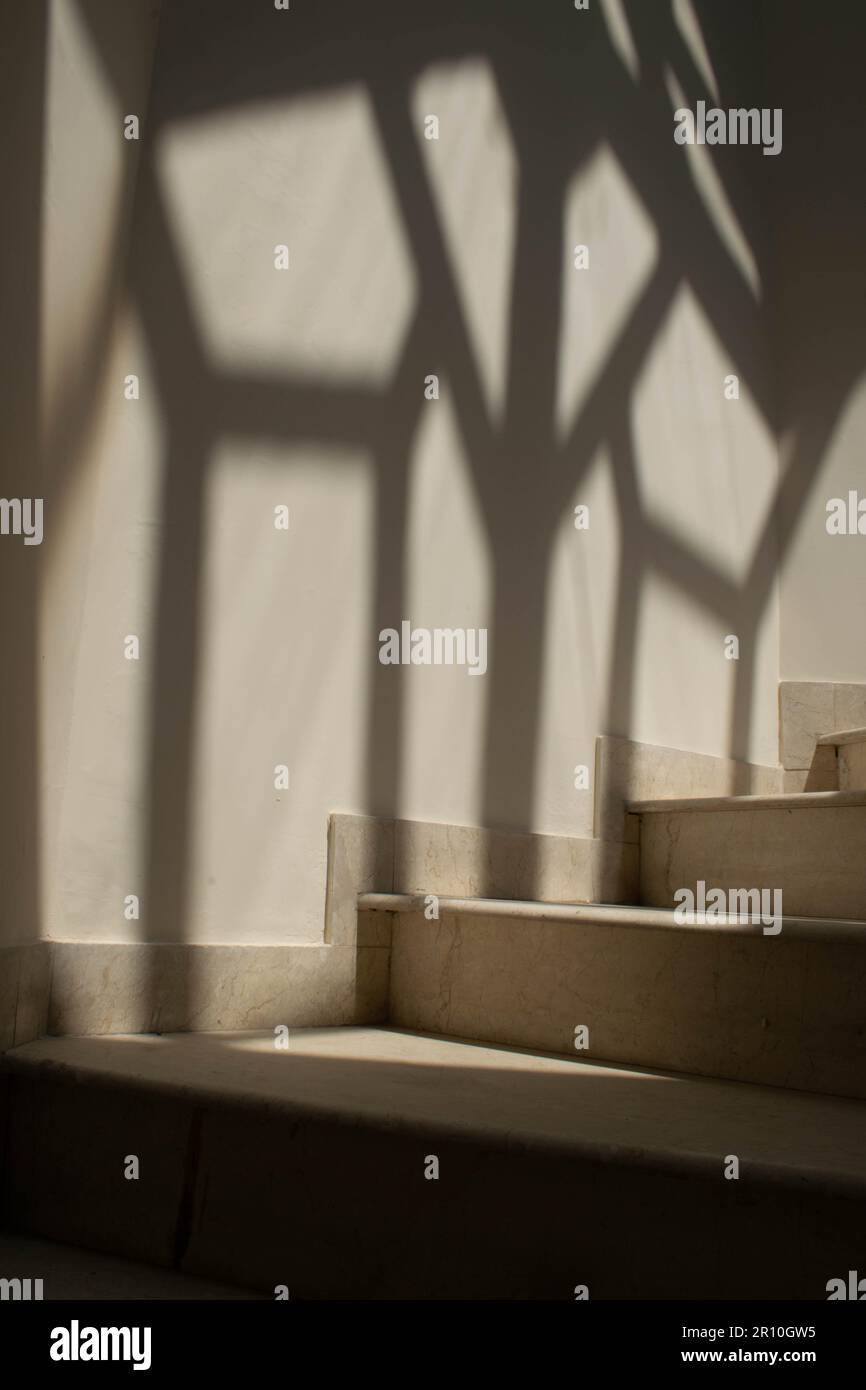 Scala a chiocciola in marmo bianco e una bella ombra artistica a forma di diamante sulla parete sul lato delle scale o sullo sfondo. Foto Stock