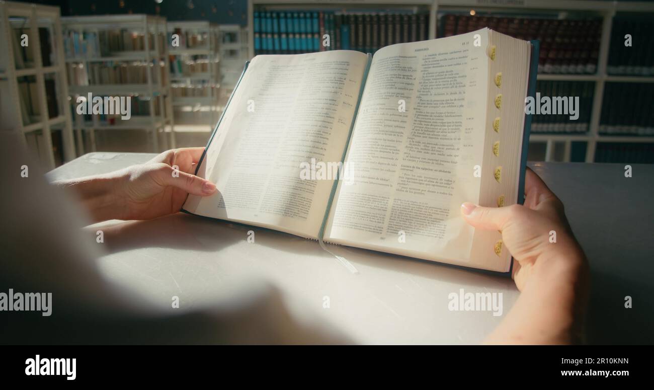 Studente autodidatta a leggere un libro nella biblioteca universitaria. Le mani femminili tengono un libro di carta aperto. Imparare studiare concetto di istruzione. Primo piano lento Mot Foto Stock