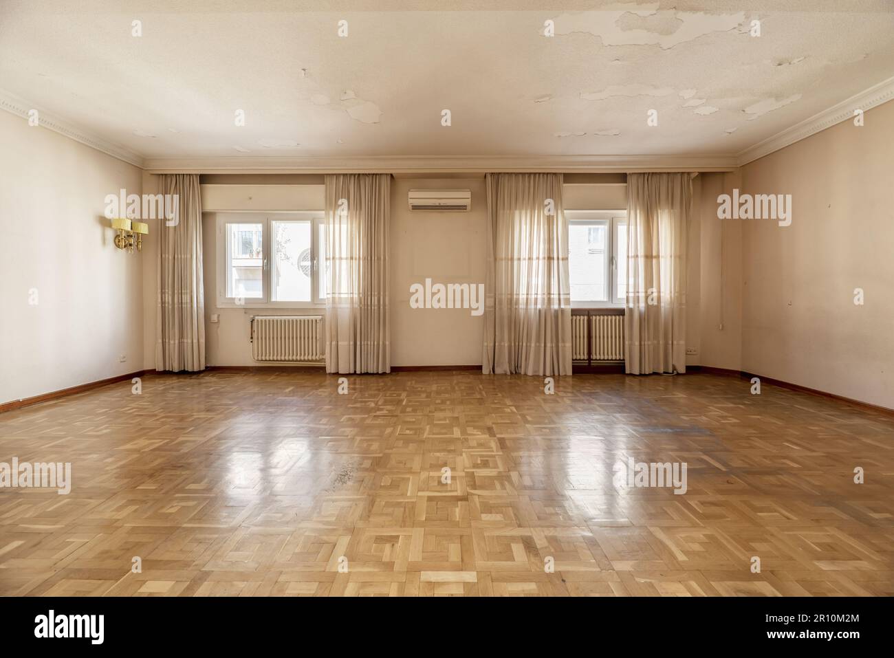 Una casa vuota con un ampio soggiorno con diverse finestre a drappo e pavimenti in parquet di quercia francese che necessitano di stabbiatura e verniciatura Foto Stock