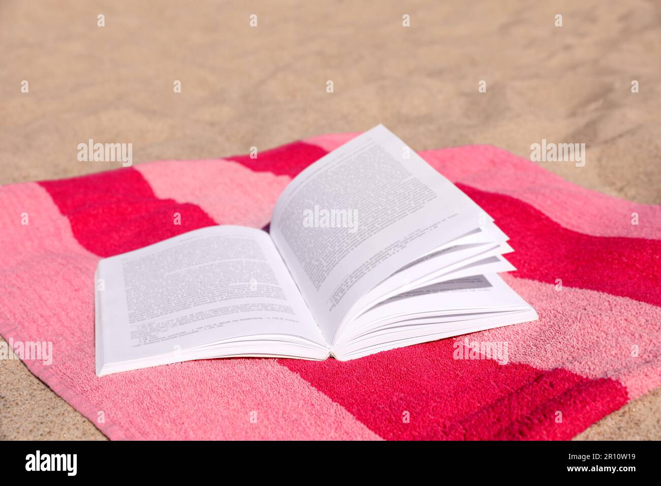 Libro aperto e asciugamano a strisce sulla spiaggia di sabbia Foto Stock