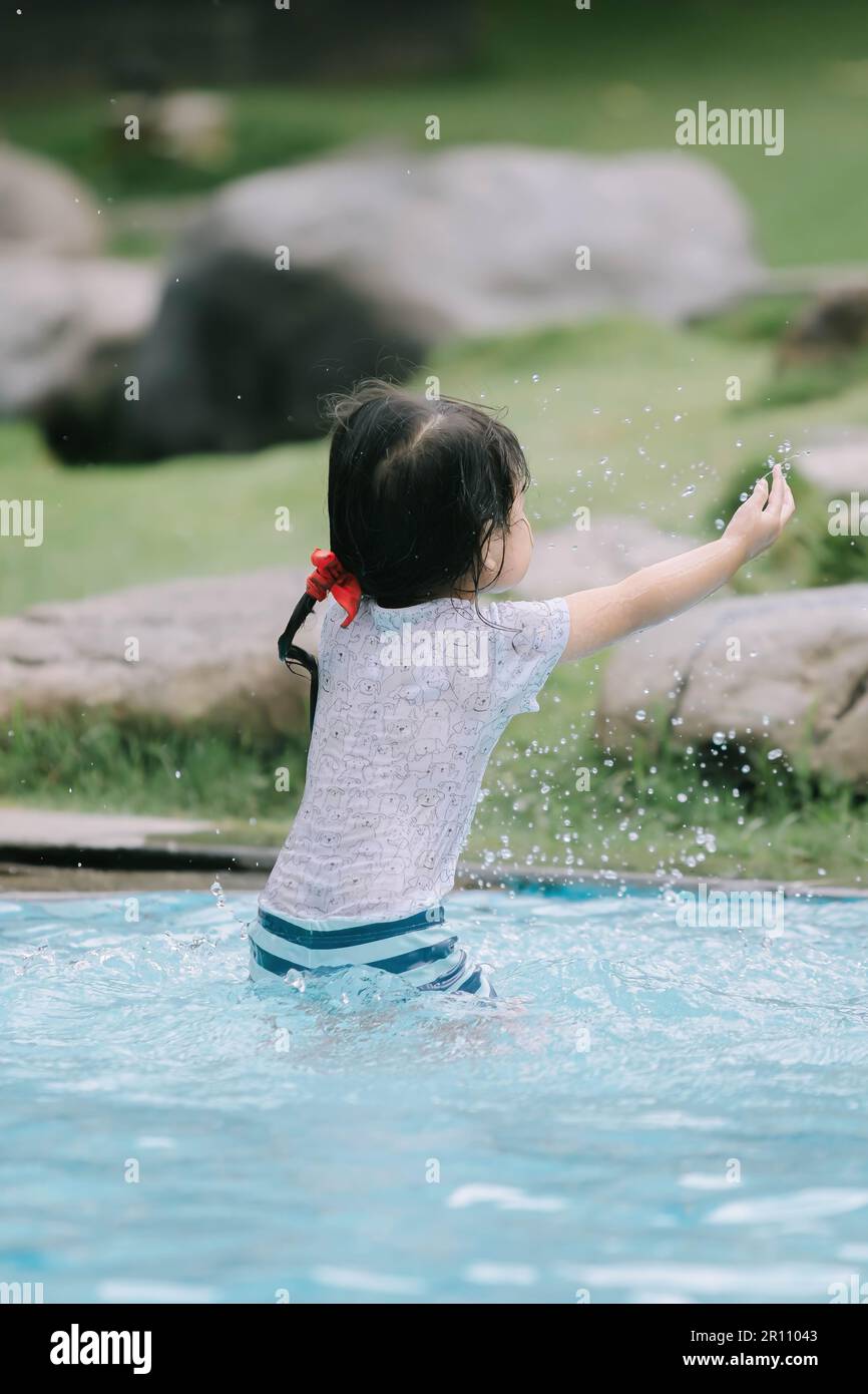 Una bambina asiatica sta spruzzando acqua nella piscina, stretta profondità di campo Foto Stock