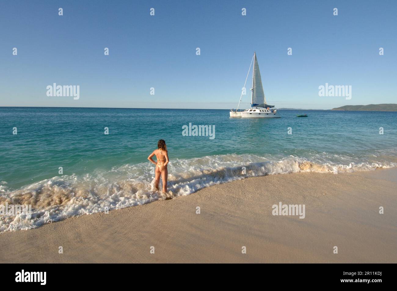 Donna in spiaggia che guarda barca a vela, vacanze al mare, vacanze, barca, barca a vela, marinaio, catamarano, mare del sud, spiaggia da sogno Foto Stock