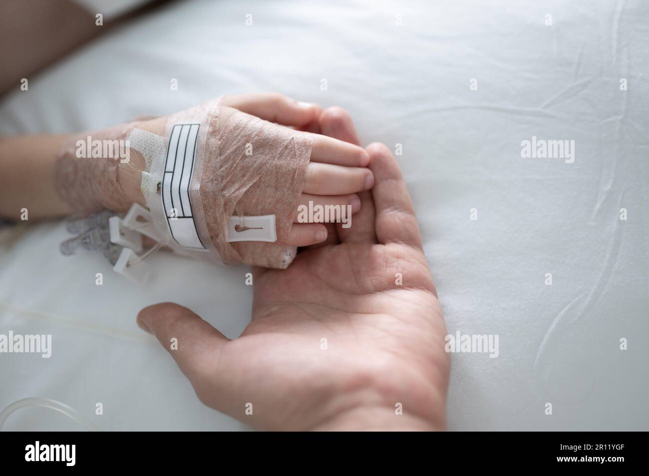 Supporto familiare del bambino in tema clinico. Man mano tenere le dita di figlia con flebo vista ravvicinata Foto Stock