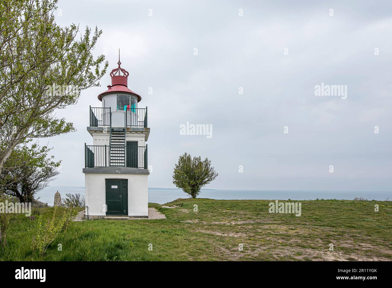 Faro di Spodsbjerg che si affaccia su un prato verde spiaggia e il mare in lontananza, Hundested, Danimarca, 10 maggio 2021 Foto Stock
