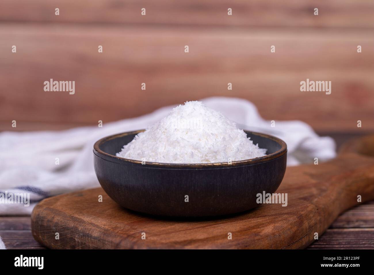 Polvere di cocco. Fiocchi di cocco messi a terra su pavimento in legno. Ciotola scura di cocco essiccato Foto Stock