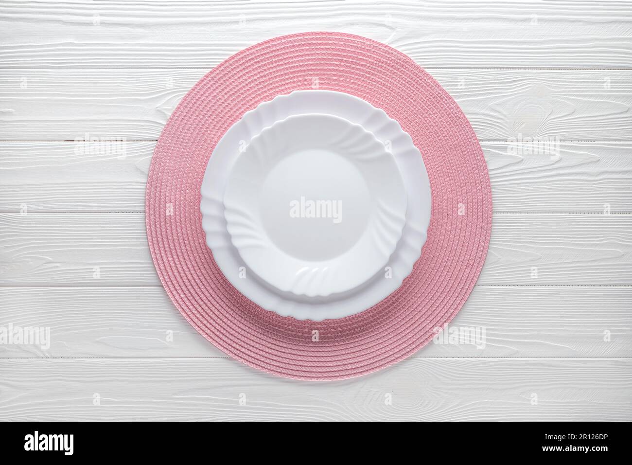 Piatto vuoto e tovagliolo rosa rotondo su un tavolo di legno bianco. Vista dall'alto. Modello di cibo, spazio di copia. Design piatto, mockup. Layout, cornice. Posizionamento, servi Foto Stock
