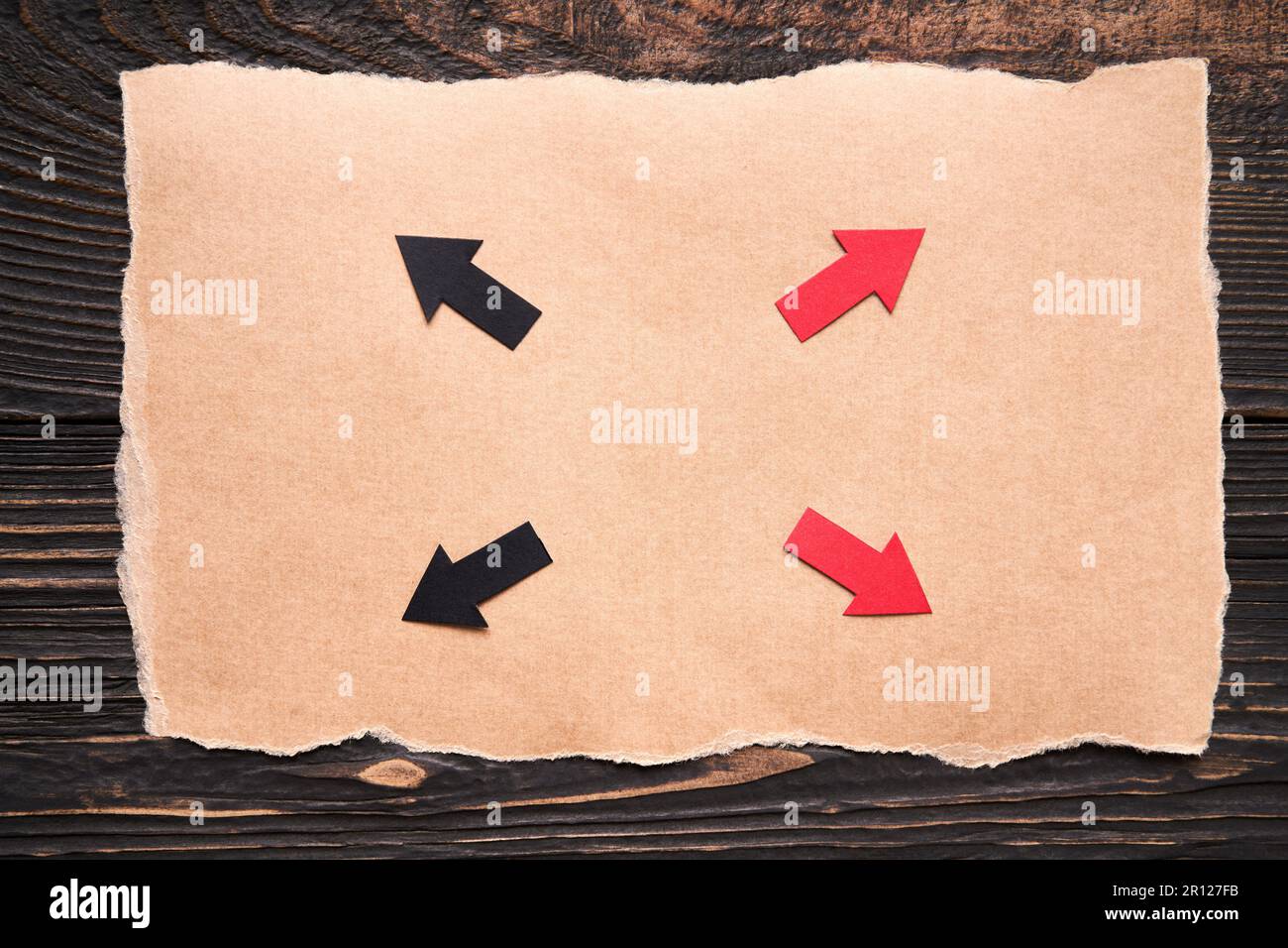 Frecce colorate sul pezzo di carta strappato su sfondo di legno scuro. Direzione, soluzione, idea Foto Stock