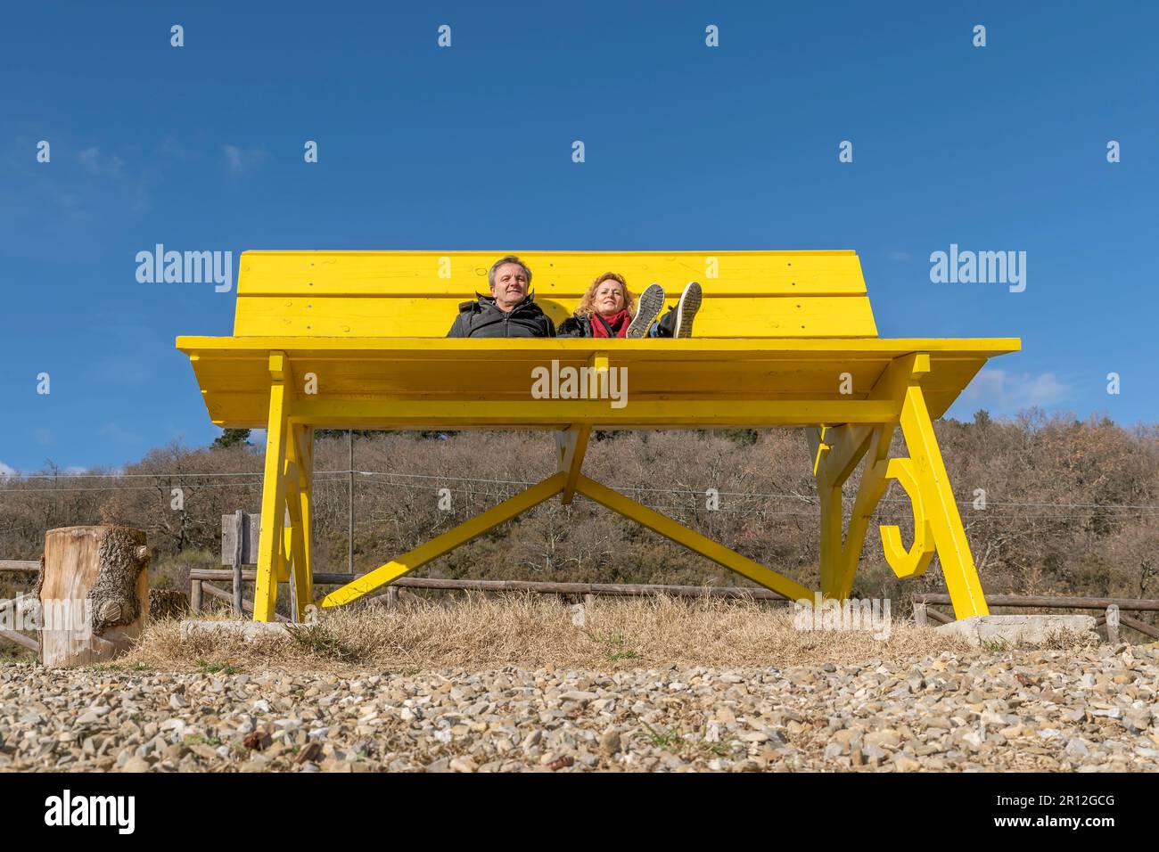 Una coppia di mezza età è seduta su una panca gialla gigante circondata dalla natura Foto Stock